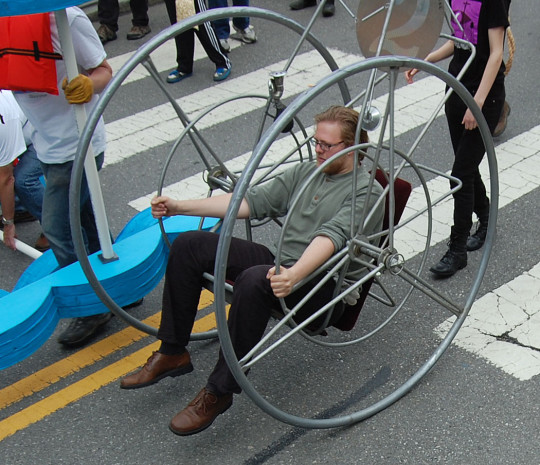 “Wheel #2” was made by Bill Wainwright for the 1982 sculpture race and will be entering the permanent collection of the MIT Museum on Monday, race organizer Christian Herold said. His nephew, James Herold, who piloted it today, said, “It’s kind of like a cantilevered wheelchair with just two wheels. You have these smaller hand wheels that you move to go. It’s got a 0-degree turning radius. You can get up to some pretty significant speeds in this but the faster you go, the less control you have so you really don’t want to do that.” (Greg Cook)